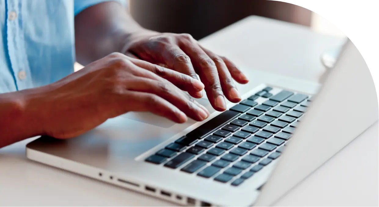 A person wearing a light blue shirt types on a silver laptop, delivering quality service with every keystroke. The image focuses on the hands and keyboard, while the background is blurred to emphasize the activity and commitment to better benefits for users.